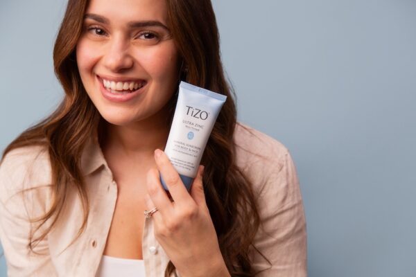 Woman smiling and holding blue product bottle by her face